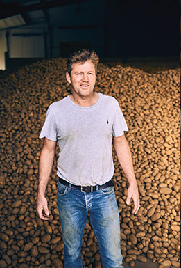 Kartoffelbauer vor einer gro&szlig;en Menge Kartoffeln in einer Lagerhalle (Foto)