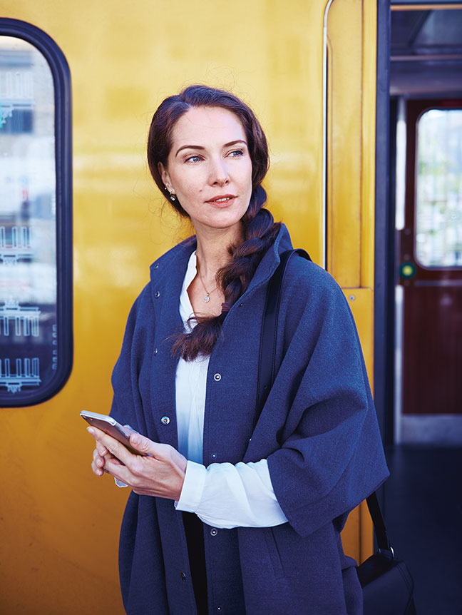 Frau mit Mobiltelefon vor einem &ouml;ffentlichen Verkehrsmittel (Foto)