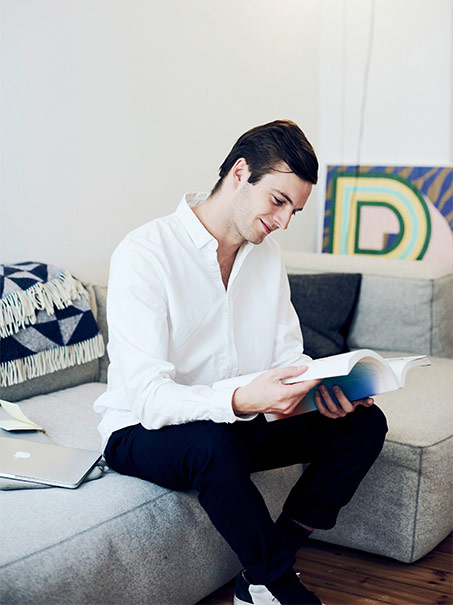 Man with book sitting on a bed (photo)