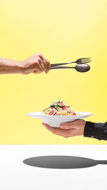 Colorful meal presented in a white plate carried by a hand; second hand carries cutlery over the plate (photo)